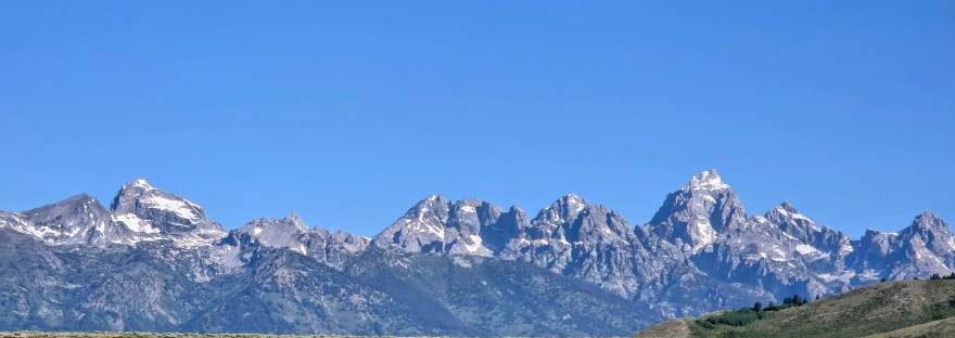 Grand Tetons - blue sky with jagged mountain peaks and green grass in the foreground
